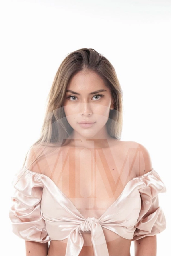 Gloria wearing a pink silk crop top tied in a knot. She gazes directly into your eyes.